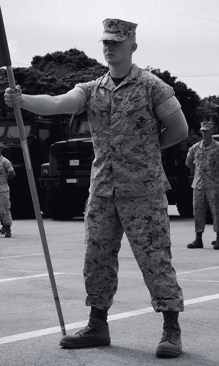 Ian Daily in Marine Corps utilities, holding a guidon at a unit formation